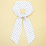 White scarf with navy blue polka dots on a beige background
