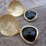 Pair of gold earrings with black stones on a wooden surface