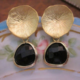 Gold earrings with black stones on a decorative plate