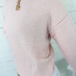 Pink sweater with gold chain necklace on a light blue background