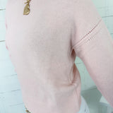 Pink sweater with gold chain necklace on a light blue background