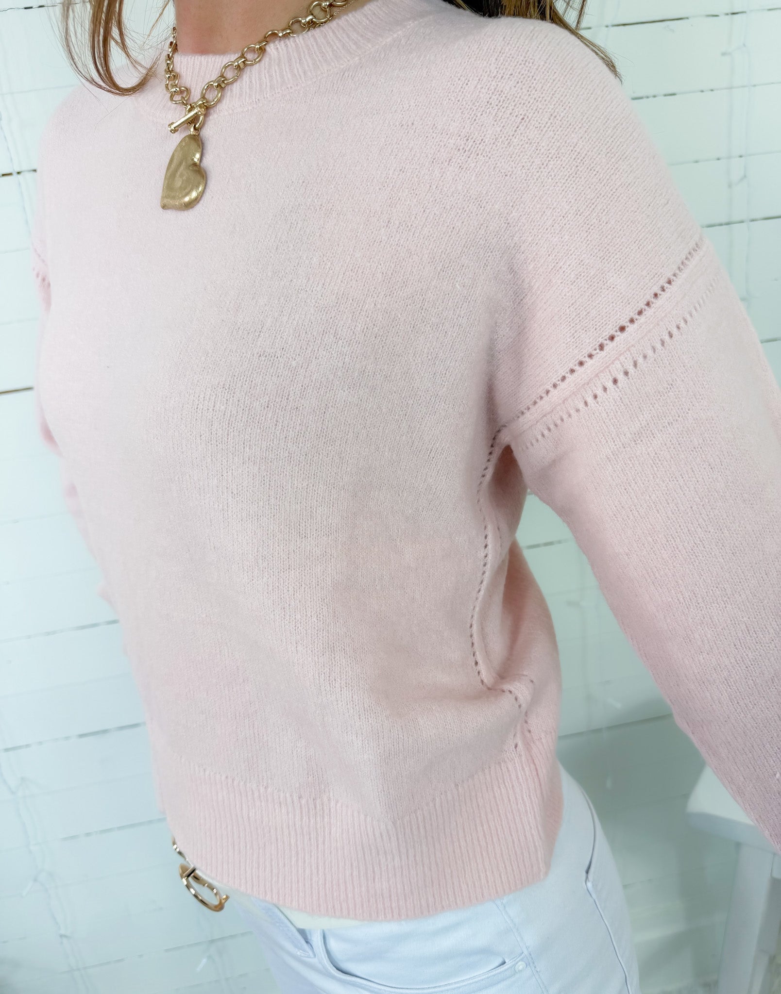 Pink sweater with gold chain necklace on a light blue background