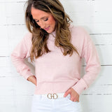Woman wearing a pink sweater and light blue jeans against a white wooden background