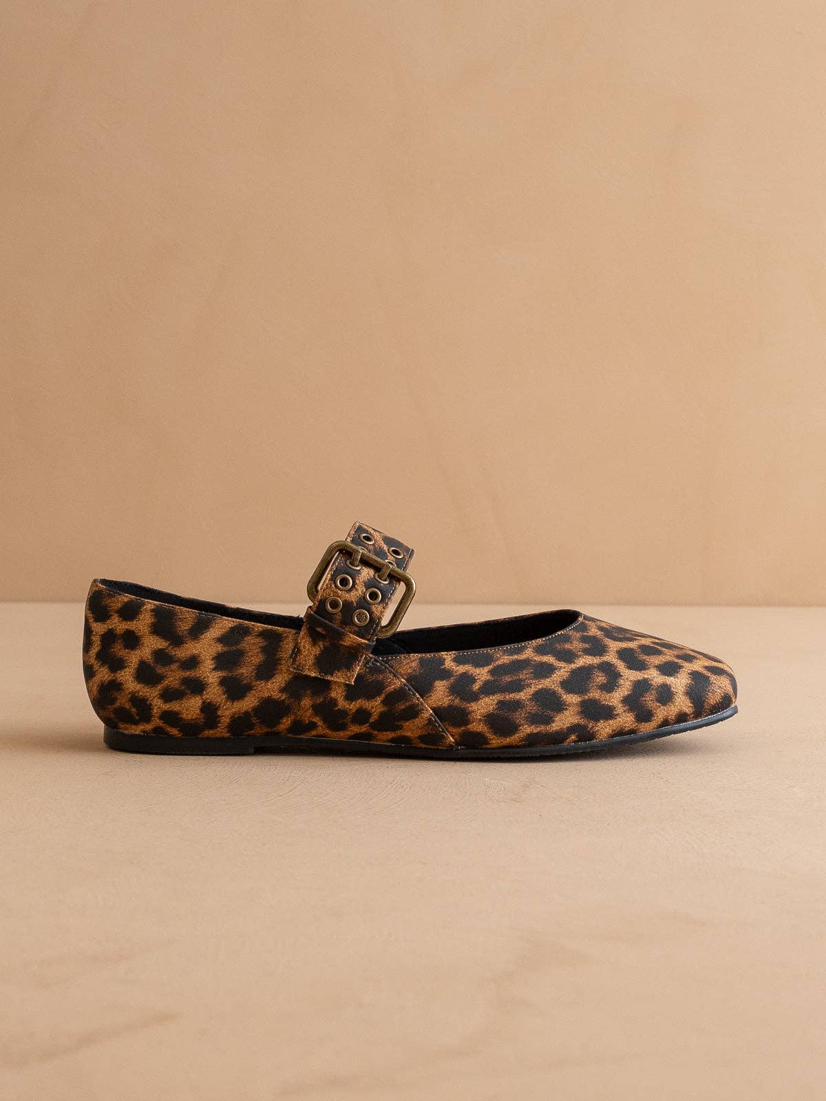 Leopard print flat shoe with a buckle on a beige background