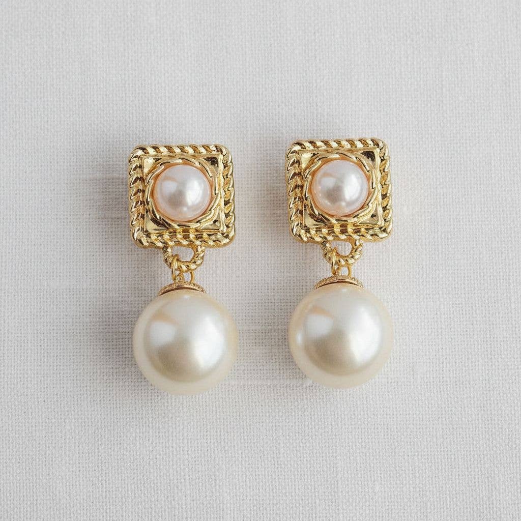 Pair of gold-framed pearl earrings on a light gray background