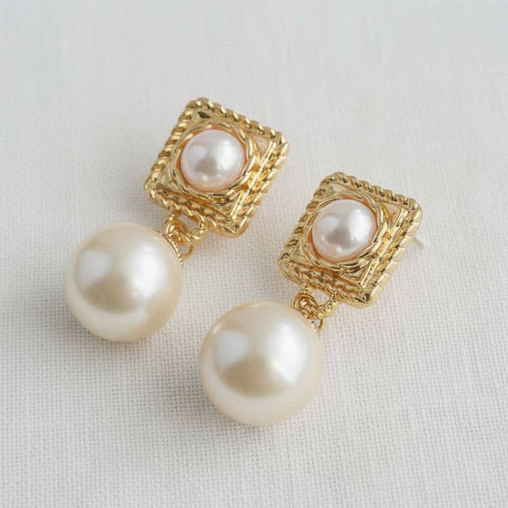 Pearl earrings with gold square frames on a light background