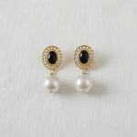 Pair of earrings with gold frames, black stones, and pearl drops on a white background
