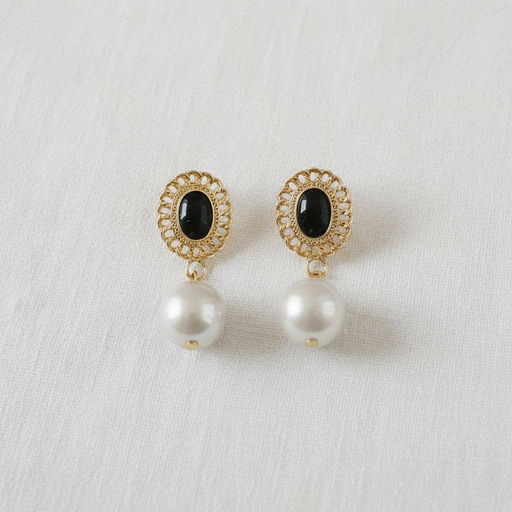 Pair of earrings with gold frames, black stones, and pearl drops on a white background