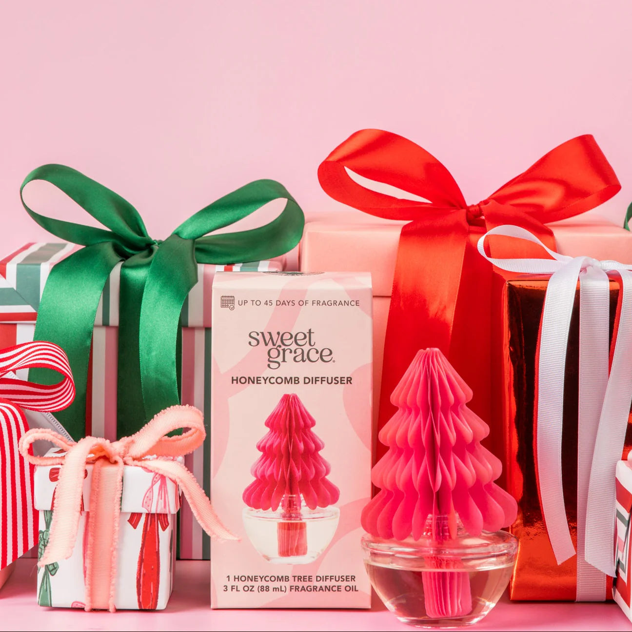 Sweet Grace honeycomb tree diffuser with wrapped gifts on a pink background