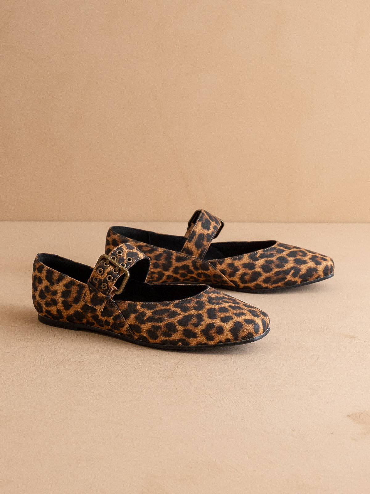 Pair of leopard print shoes with buckles on a beige background