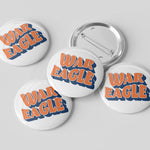 Five round pin-back buttons on a light gray background, with four showing the front design and one showing the metal pin-back back. The front design features the words 'WAR EAGLE' in orange with a blue shadow outline on a white button face.