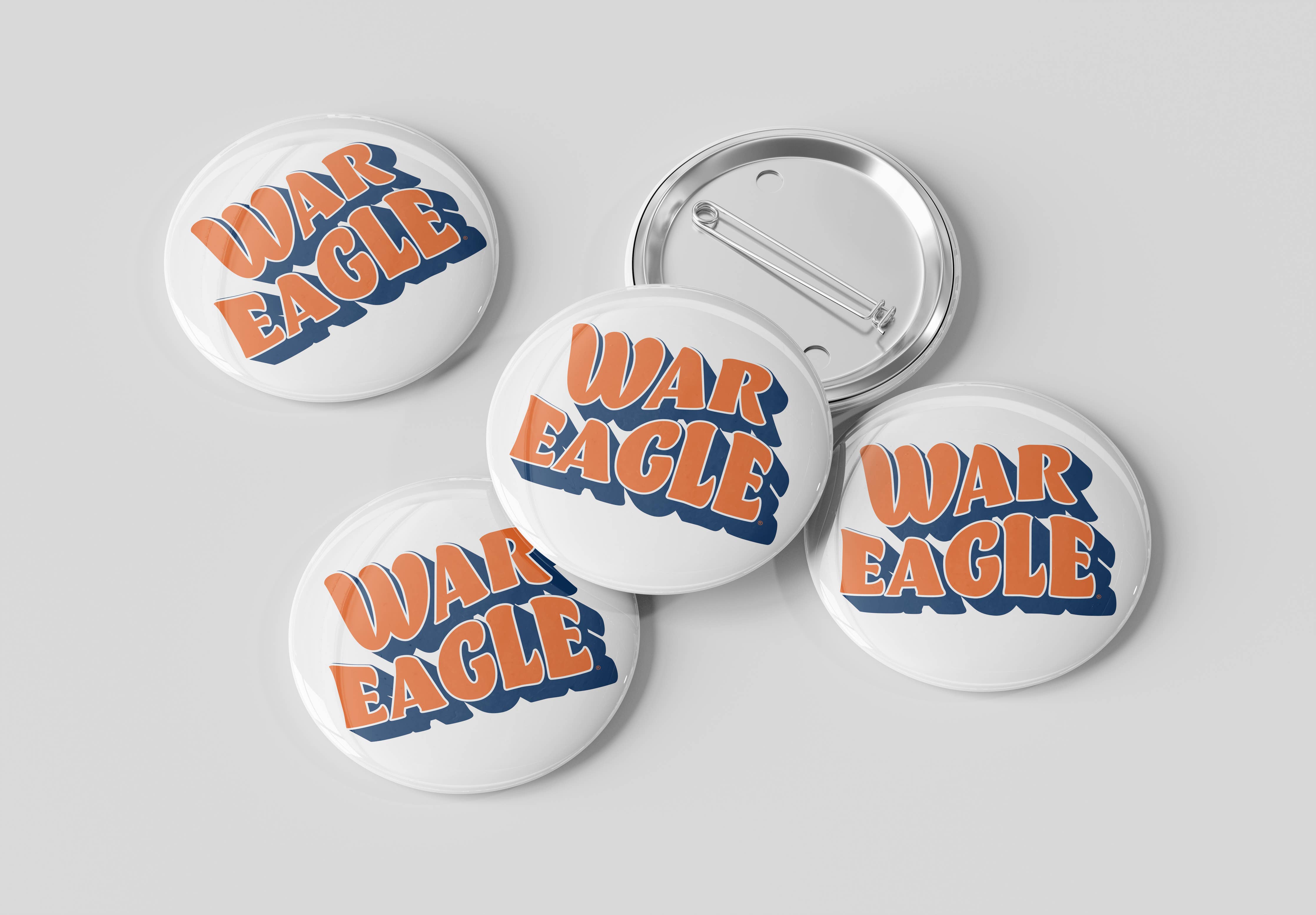 Five round pin-back buttons on a light gray background, with four showing the front design and one showing the metal pin-back back. The front design features the words 'WAR EAGLE' in orange with a blue shadow outline on a white button face.