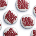 Several round white button badges with the words "ROLL TIDE" in large red stylized lettering, arranged on a light gray background.