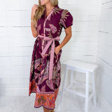 Woman wearing a patterned dress standing in a room with white walls and a white stool.