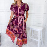 Woman wearing a patterned dress standing against a white wooden panel background