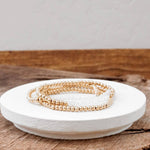 A stack of gold-tone glass bead bracelets on a white plate, with a wooden surface in the background.