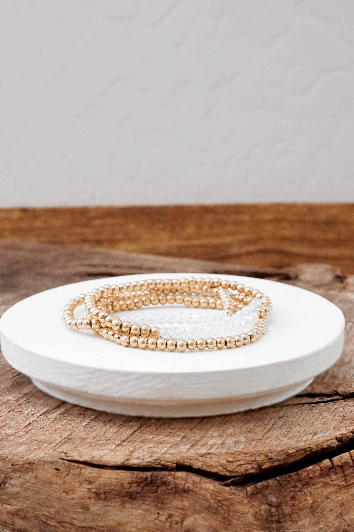 A stack of gold-tone glass bead bracelets on a white plate, with a wooden surface in the background.