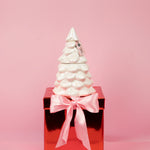 White ceramic Christmas tree on a red box with a pink ribbon against a pink background