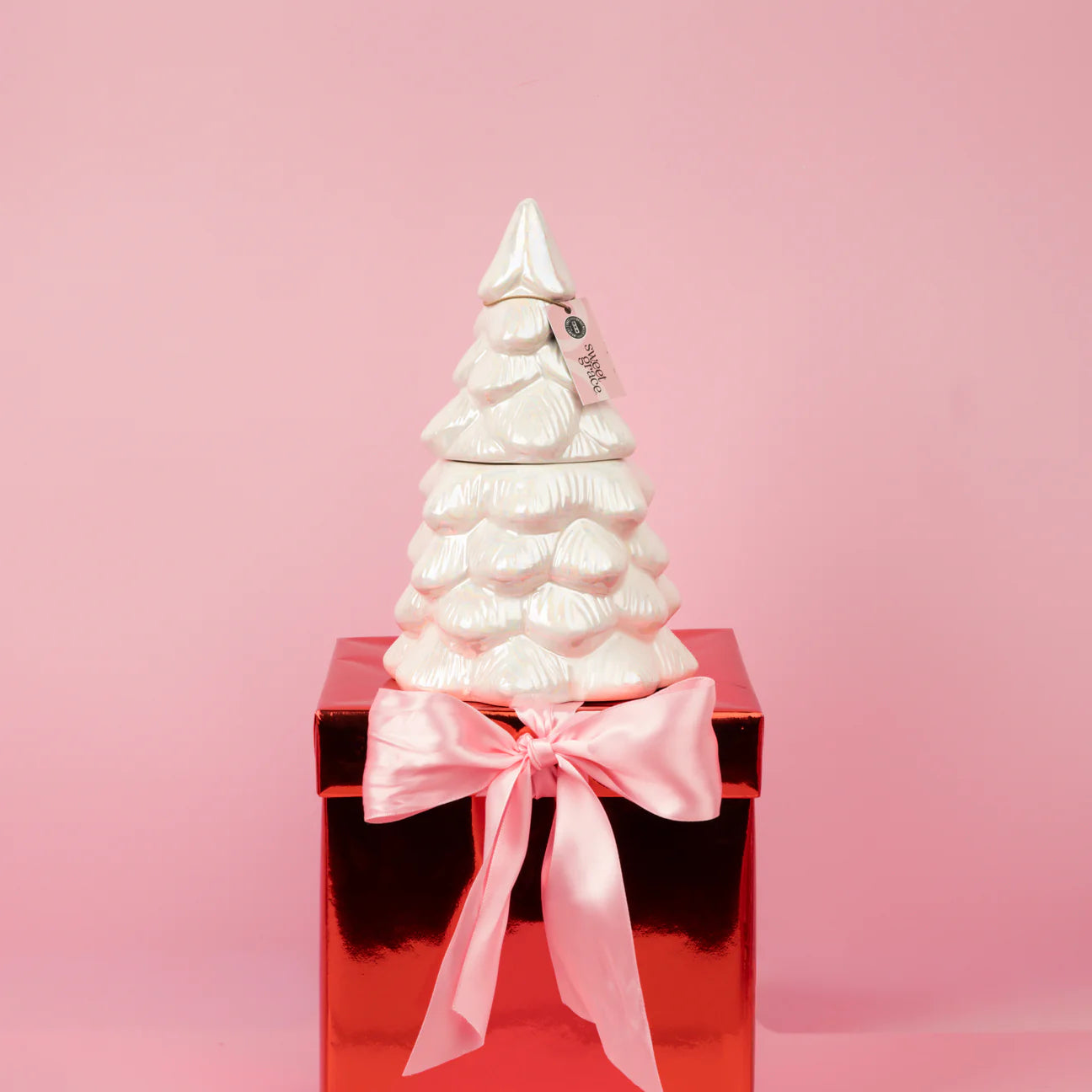 White ceramic Christmas tree on a red box with a pink ribbon against a pink background