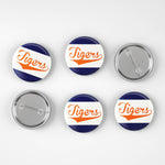 Six round pin-back buttons on a light gray background, showing both the front and back views. The front faces feature a navy blue and white diagonal striped design with the word 'Tigers' in orange script.