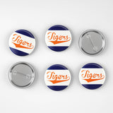 Six round pin-back buttons on a light gray background, showing both the front and back views. The front faces feature a navy blue and white diagonal striped design with the word 'Tigers' in orange script.