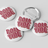 Four round pin-back buttons with a white face and red retro-style text reading 'ROLL TIDE,' plus one button showing the silver metal pin back, arranged on a light gray background.