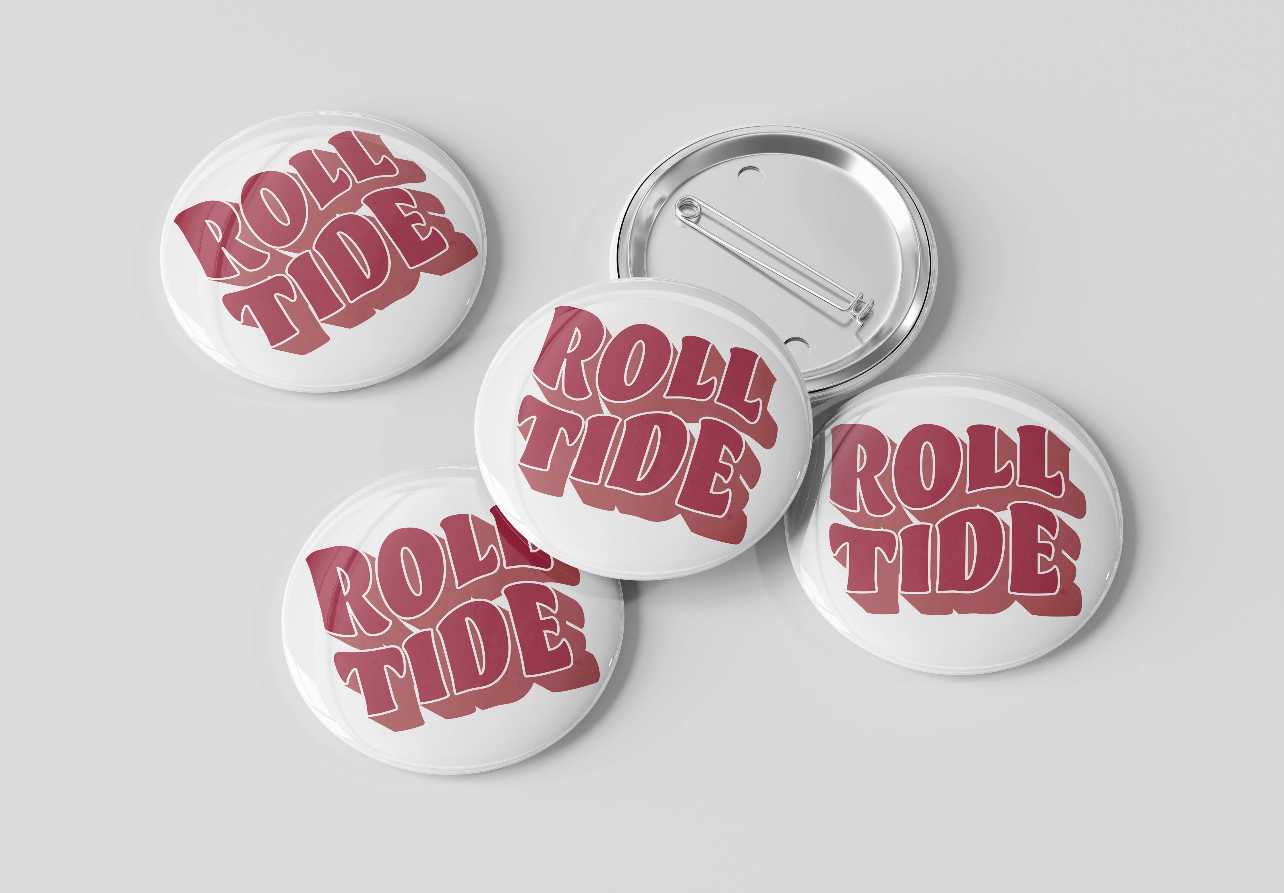 Four round pin-back buttons with a white face and red retro-style text reading 'ROLL TIDE,' plus one button showing the silver metal pin back, arranged on a light gray background.