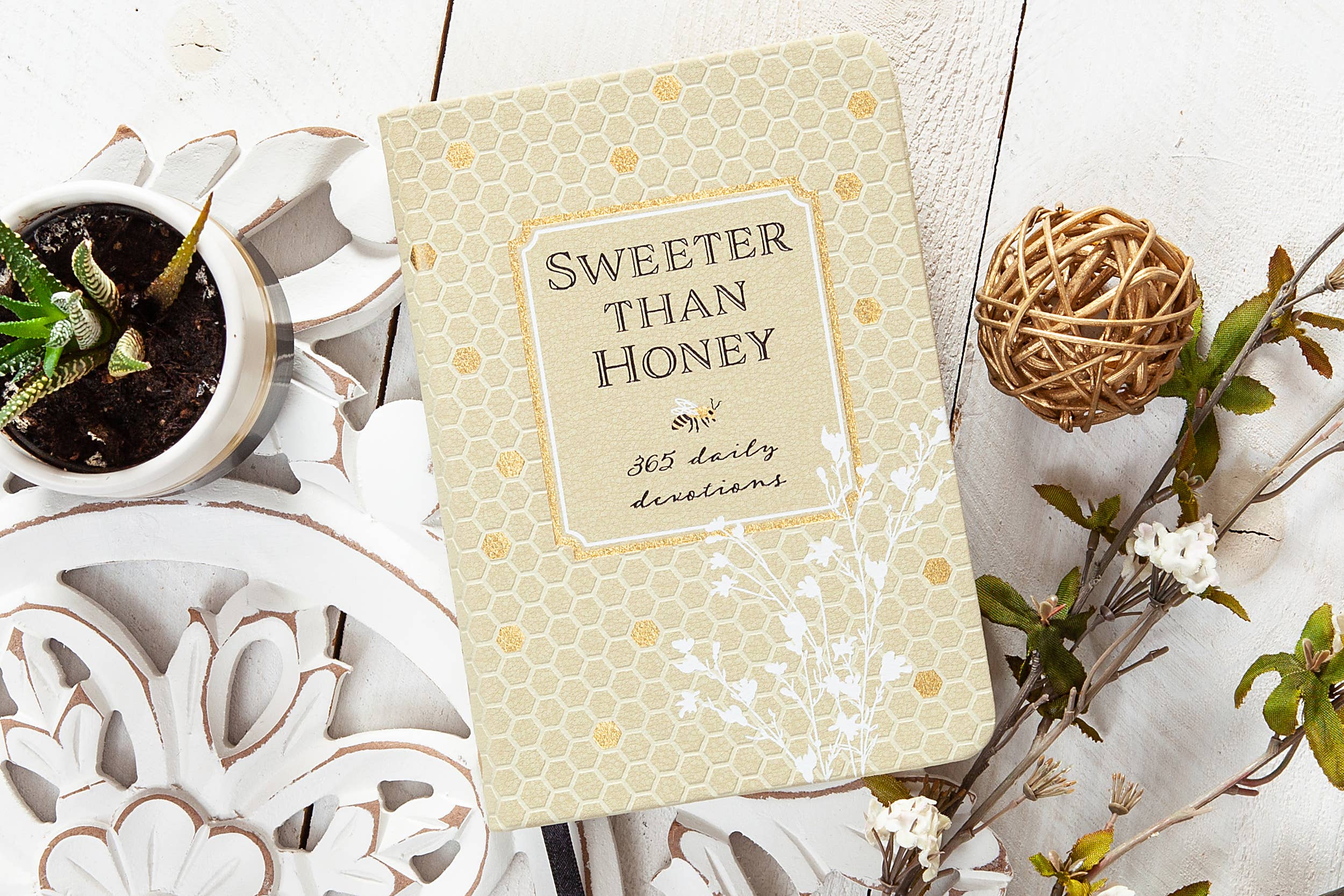 Book titled 'Sweeter Than Honey' on a decorative surface with plants and balls.