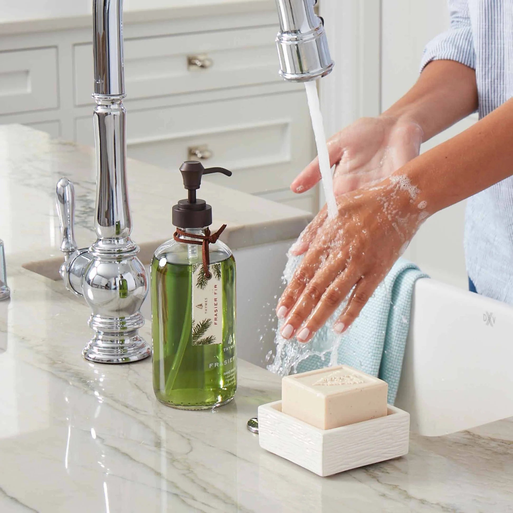 Person washing hands with soap and water in a kitchen sink.