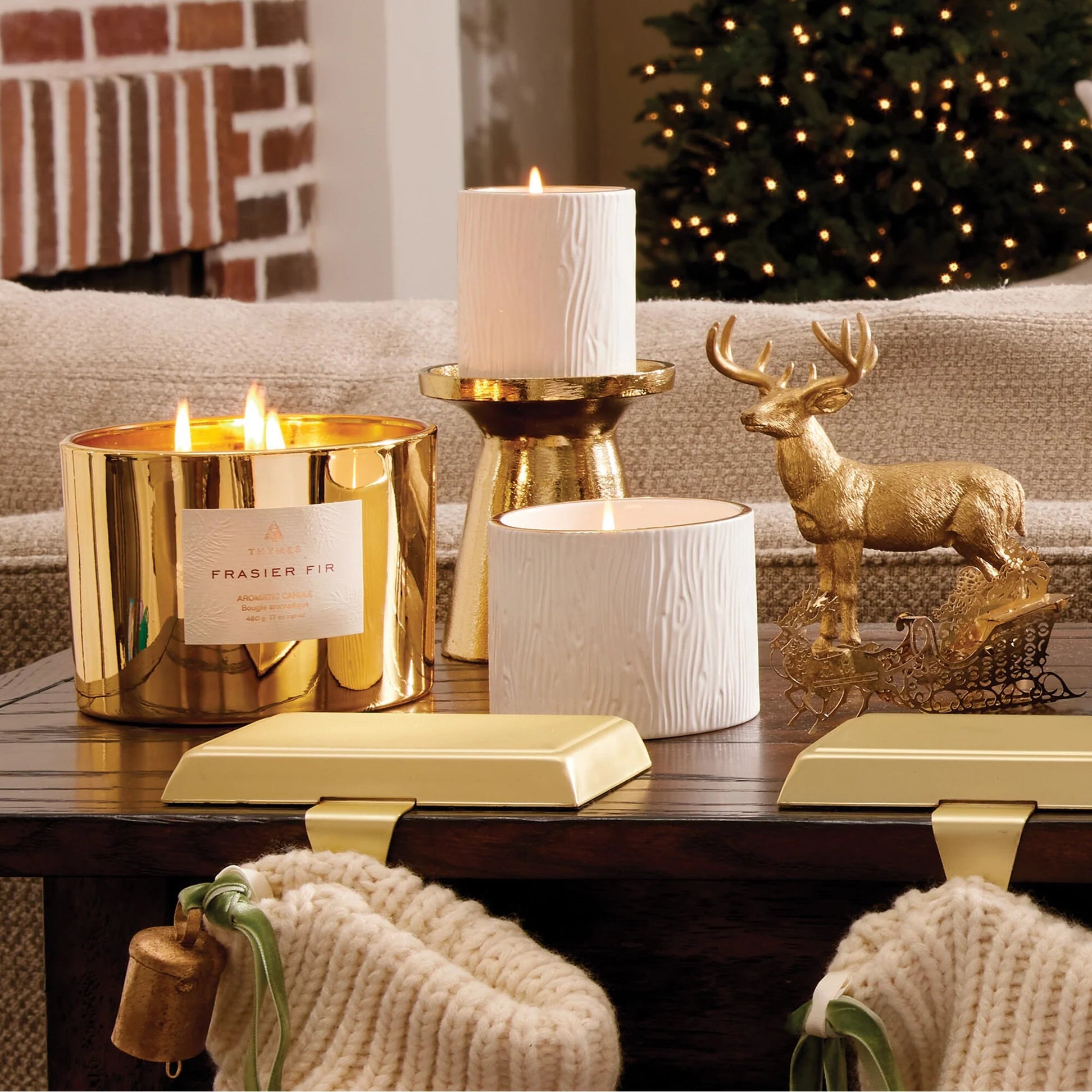 Decorative candles and a deer figurine on a table with a Christmas tree in the background.