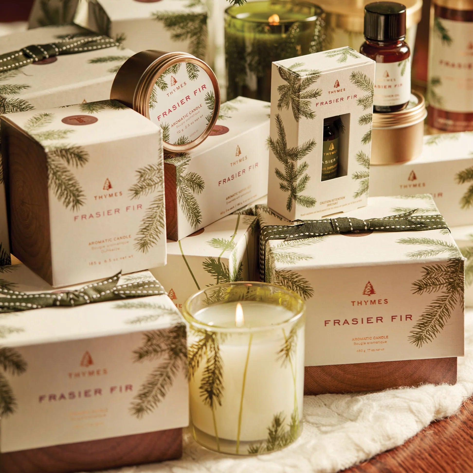 Thymes Frasier Fir candles and packaging on a decorative surface with greenery.