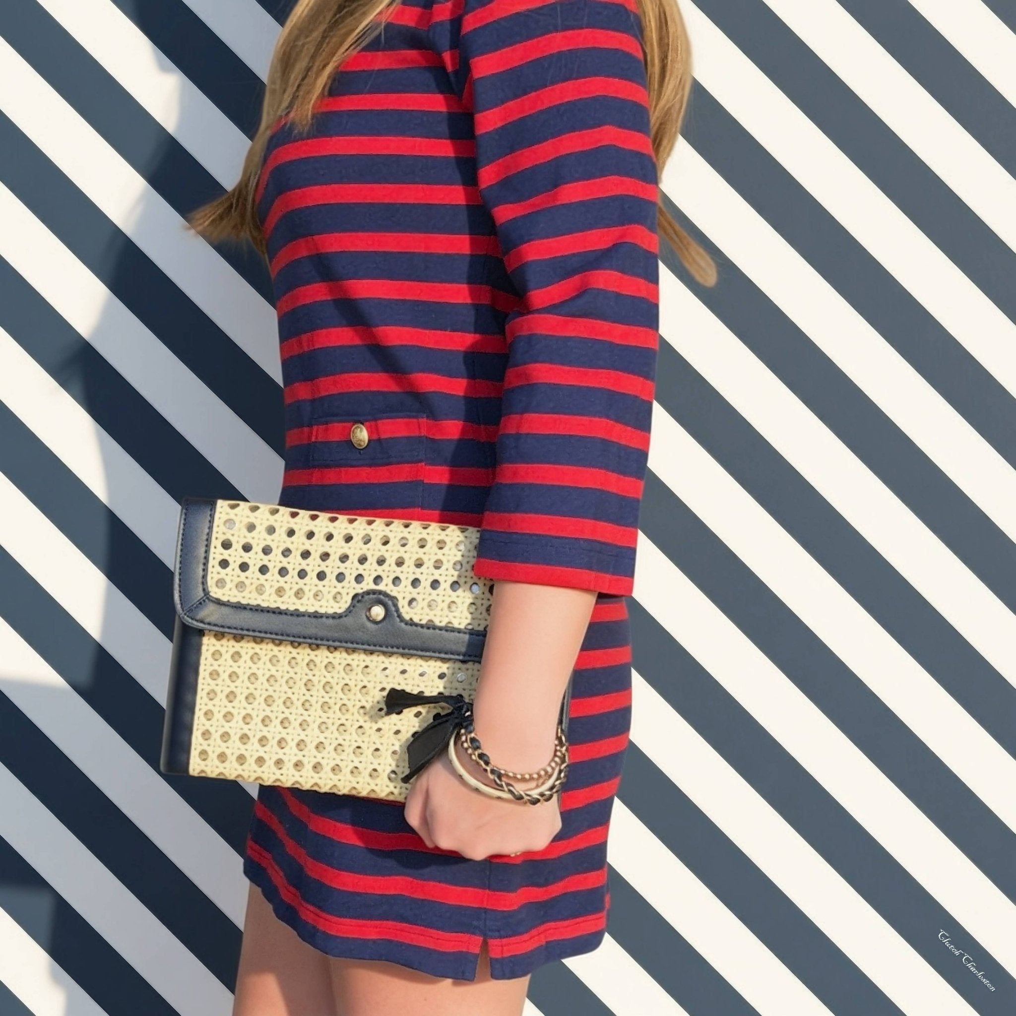 Person wearing a red and blue striped dress holding a gold clutch against a striped background