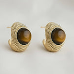 Pair of gold hoop earrings with brown gemstones on a light gray background