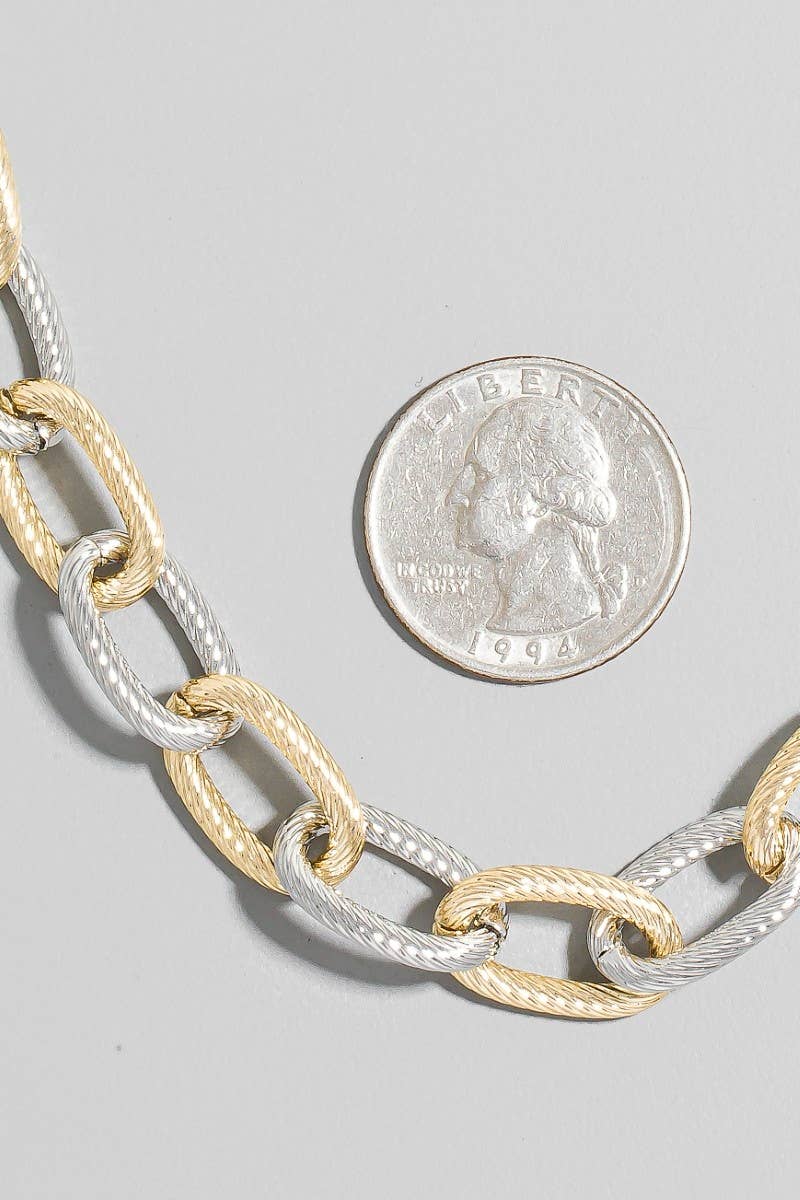 Two-toned chain necklace with a quarter for scale on a gray background
