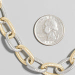 Two-toned chain necklace with a quarter for scale on a gray background
