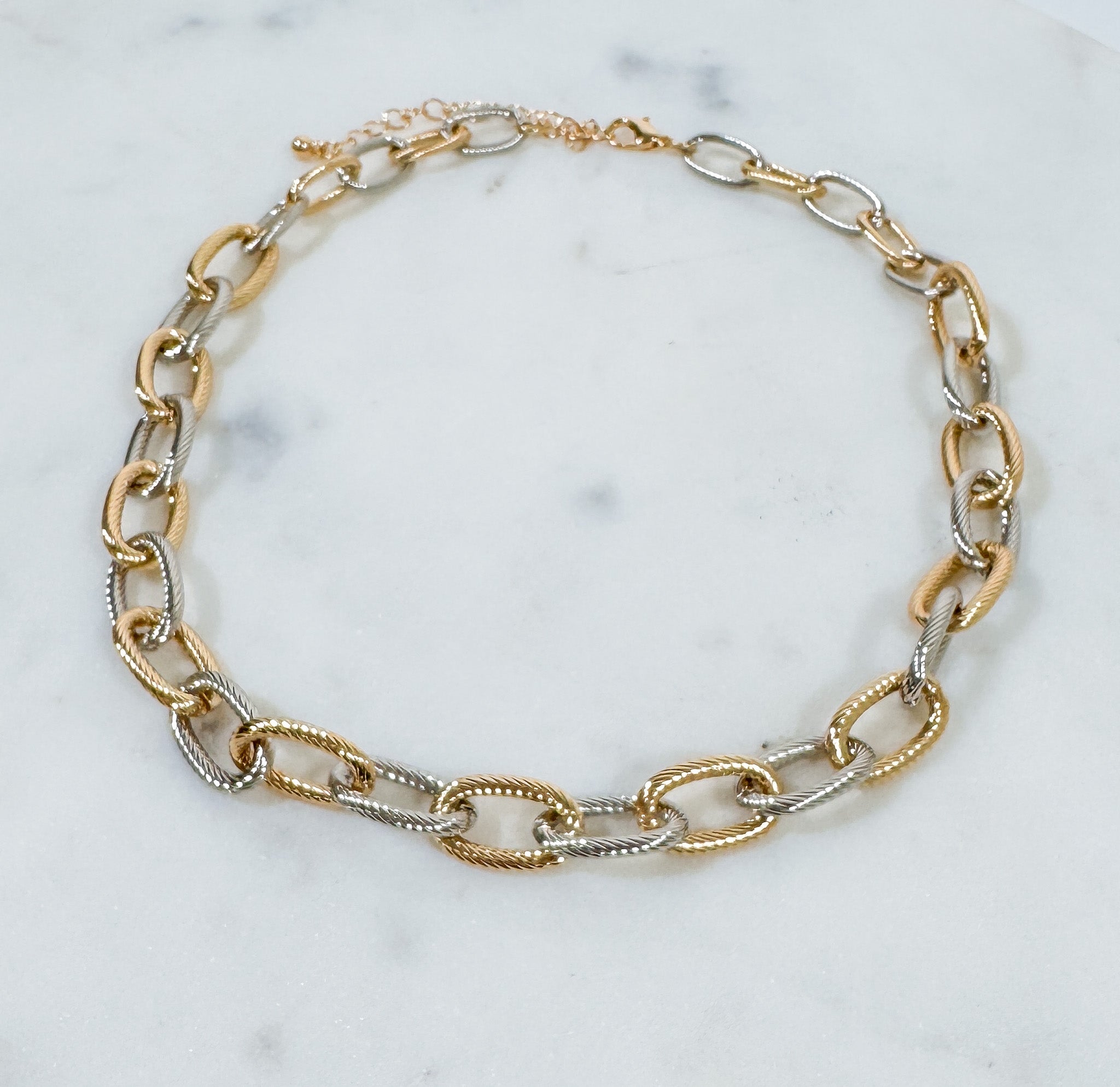 Gold and silver chain bracelet on a marble surface