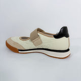 A women's Mary Jane style shoe in cream, beige, and black, featuring a hook-and-loop strap closure and a brown outsole, shown from a side profile on a white background.