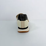 A single low-top shoe shown from the back, featuring an off-white leather upper with a black leather heel tab, a black horizontal stripe, and a tan sole.