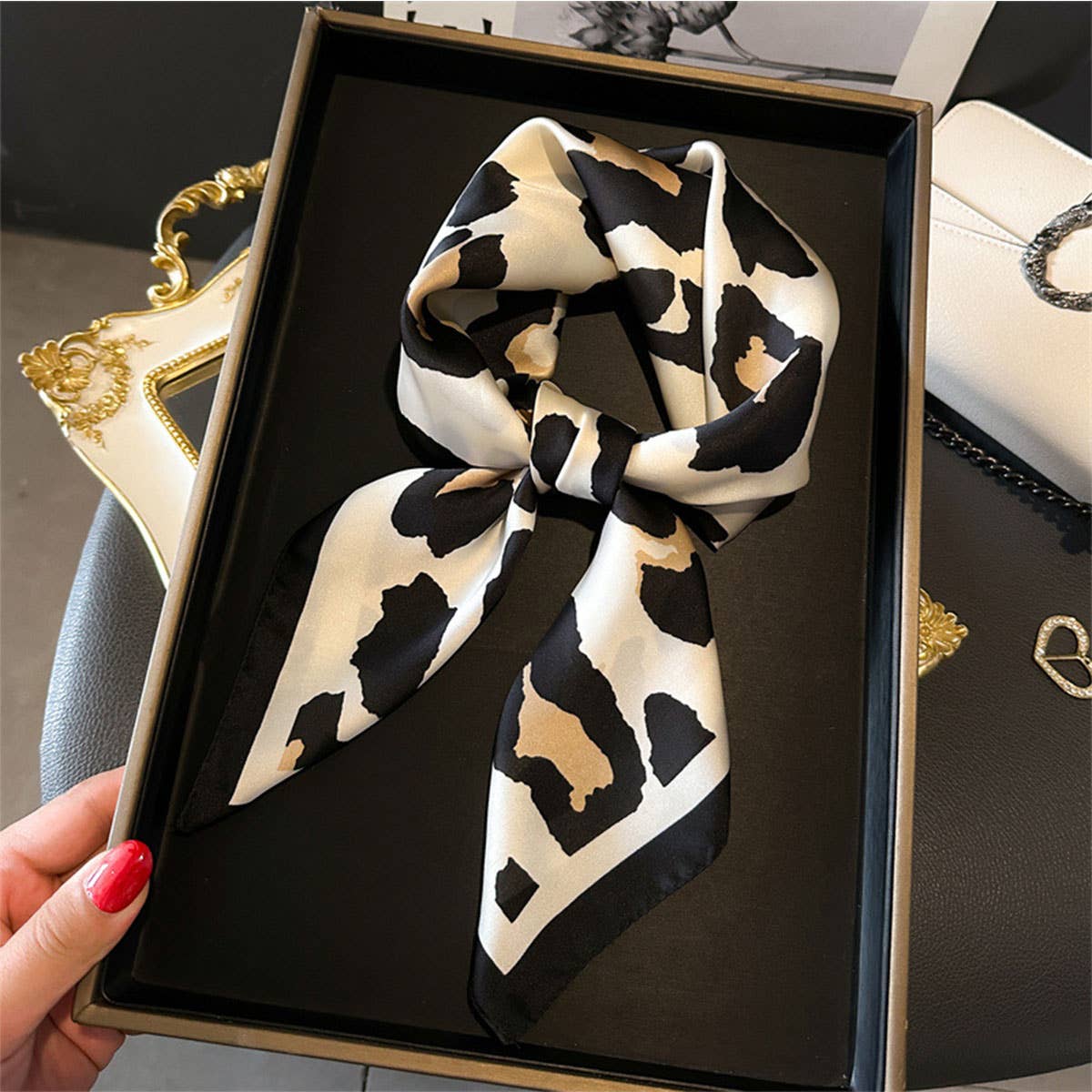 Black and white patterned scarf in a decorative box held by a hand with red nail polish.