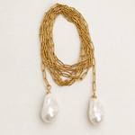A gold chain necklace featuring two large, irregular white baroque pearls hanging from the ends, displayed on a light beige textured background.