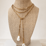A gold-toned multi-strand necklace with two large white shell-like pendants, displayed on a beige fabric-covered jewelry bust against a light neutral background.