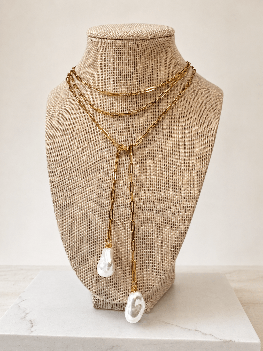 A gold-toned multi-strand necklace with two large white shell-like pendants, displayed on a beige fabric-covered jewelry bust against a light neutral background.