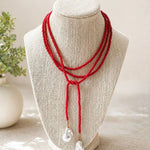 A red multi-strand beaded necklace with two white baroque pearl drop pendants, displayed on a beige fabric jewelry bust.