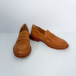 A pair of tan leather penny loafers with low stacked heels, displayed on a clean white studio background.