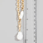 Gold chain necklace with white pearls next to a ruler on a gray background