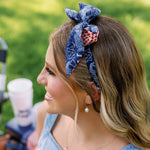 A woman outdoors wearing a blue patterned fabric headband with a red and white polka dot accent, paired with a light blue denim top.
